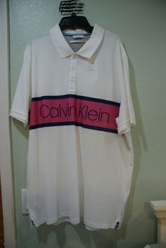 115 Men's Calvin Klein Short Sleeve White with Logo 3 Front Buttons Polo Shirt--XXL--Brand New!! This is one very nice Calvin Klein shirt has the logo in Pink and Blue Silk Screened on the front of the shirt and is of great design and detail given to it. Collared Cotton Shirt With Logo Print, Collared Cotton Shirt With Logo, Cotton Collared Shirt With Logo Print, Cotton Collared Top With Logo Print, Classic Calvin Klein Shirt For Summer, Classic Calvin Klein Summer Shirt, Calvin Klein White Short Sleeve Top, Calvin Klein Cotton Summer Shirt, Classic Calvin Klein Short Sleeve T-shirt