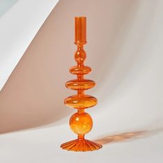 an orange glass candle holder sitting on top of a white table next to a wall