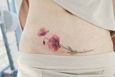 a woman's lower back tattoo with pink flowers on her left side ribcage