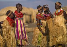 three women in traditional african dress standing next to each other with straw huts behind them