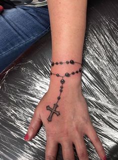 a woman's hand with a rosary tattoo on her left wrist and the cross tattooed on it