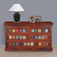 a wooden dresser with multicolored tiles on the front and sides, next to a lamp