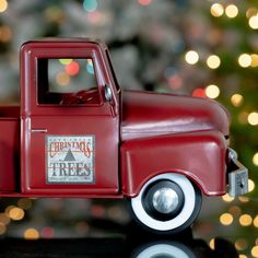 a red toy truck sitting on top of a table next to a christmas tree with lights in the background