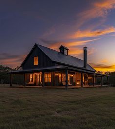 a large house sitting in the middle of a field at sunset with windows lit up