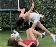 two young women are playing in the grass with an umbrella over their heads and a small white dog sitting next to them