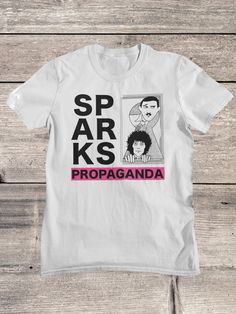 Sparks T-Shirt | Sparks Band Shirt | Glam Rock Shirt | Synth Pop  Sparks (formerly Halfnelson) is an American pop and rock duo formed by brothers Ron (keyboards) and Russell Mael (vocals) in Los Angeles. Our Shirts, hoodies and tanks have been carefully chosen after many years of testing, they are semi fitted around the chest and arms, and therefore give a complimentary look, but they also come in a nice length, Our shirts can be washed many times and the print will not fade, so you can enjoy yo White Crew Neck Rock T-shirt, White Short Sleeve Rock T-shirt, White Crew Neck Rock Style Tops, White Rock Style Cotton T-shirt, White Rock Style Top For Concerts, White Band Merch Shirt With Logo, White Band Logo Graphic Tee, White Rock Style T-shirt For Streetwear, Rock Style White Screen Print Tops