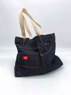 a bag made out of blue jeans with a white strap hanging from the bottom, and a red logo on the front pocket