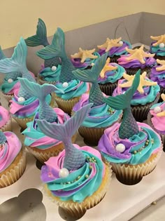 cupcakes decorated with blue, pink and purple icing are displayed on a table