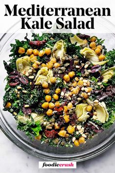 Mediterranean Kale Salad | foodiecrush.com Image shows a closeup overhead shot of a large clear glass bowl filled with massaged kale, roasted chickpeas, artichoke hearts, olives, sun-dried tomatoes, capers, and pine nuts in a lemony dressing