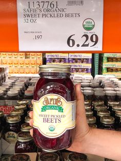 a person holding up a jar of sweet pickled beets in front of shelves