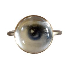 Lover's Eye ring with a round oil painting encased in gold plate over sterling with a quartz crystal cabochon which gives a magical magnifying effect, measuring 1/2"; ring size 5.5. THE HISTORY: Lover's Eyes were a jewelry trend c.1785-1830 of brooches set with tiny watercolor portraits on ivory. Since they were cropped to eyes, they were in many ways more direct and intimate than traditional miniature portraits; but also because they were just eyes, they were often used as daring public testimonies of clandestine love affairs with mystery lovers. THE SETTINGS: This piece is part of the collection of contemporary minimalist settings which juxtapose this historical jewelry tradition with clean, modern lines for a subtle effect that's easy to wear. Gold Round Mystical Moonstone Ring, Mystical Gold Round Rings, Gold Moonstone Cabochon Ring, Gold Moonstone Cabochon Ring In Sterling Silver, Gold Cabochon Moonstone Ring Collectible, Gold Moonstone Ring Collectible, Spiritual Gold Moonstone Cabochon Ring, Victorian Round Moonstone Ring For Gift, Unique Cabochon Crystal Ring