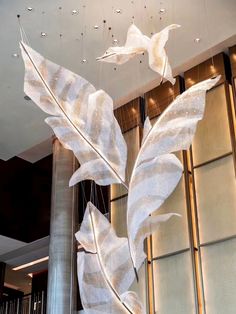 a large metal sculpture hanging from the ceiling in front of a tall glass wall with white leaves on it