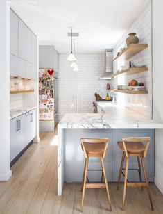 two wooden stools sitting in front of a kitchen island with marble counter tops and open shelving