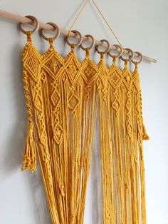 yellow macrame hanging on the wall with wooden hooks and rings attached to it