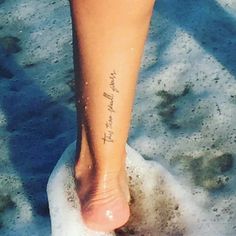 a person's foot in the sand with a small tattoo on their left leg