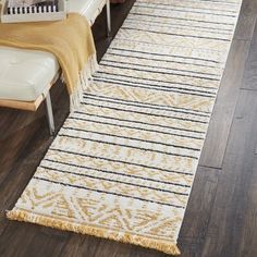 a white and yellow area rug with fringes on the floor next to a chair