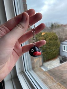 a hand holding a black and red bird keychain in front of a window