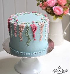 a blue cake decorated with pink flowers on a white pedestal next to a flower vase