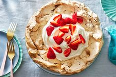 a pie topped with strawberries on top of a table next to plates and silverware