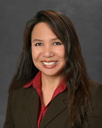 a woman with long dark hair wearing a black jacket and red shirt smiling at the camera