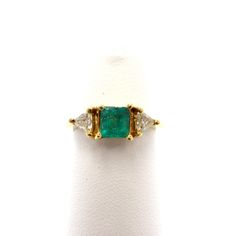 an emerald and diamond three stone ring on a white surface with gold trimmings