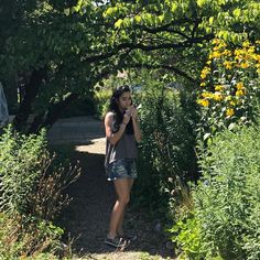 a woman is standing in the middle of some bushes and trees, talking on her cell phone