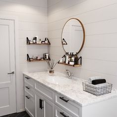 a white bathroom with two sinks and shelves on the wall next to each other in front of a round mirror