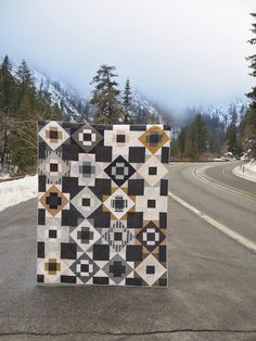 a patchwork quilt sitting on the side of a road next to snow covered mountains