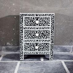 an intricately designed white and black cabinet on the ground in front of a concrete wall