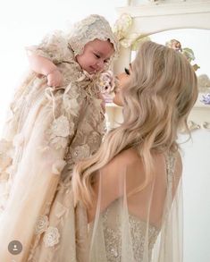 a woman holding a baby in her arms and wearing a dress with flowers on it