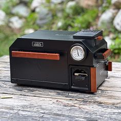 an old fashioned camera sitting on top of a wooden table next to some grass and rocks