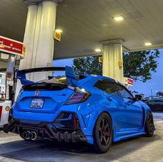 a blue sports car parked in front of a gas station with its hood open and the back lights on