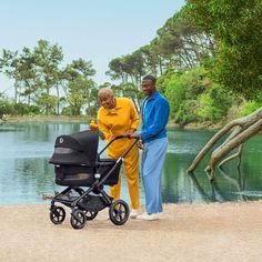 a man and woman are standing next to a baby stroller by the water,