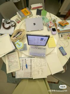 a round table covered with notebooks, papers and an apple laptop on top of it