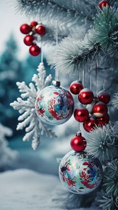 christmas ornaments hanging from the branches of a tree in front of snow covered pine trees