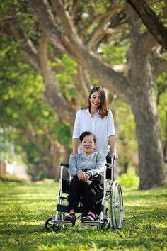 a woman pushing a boy in a wheel chair through the grass with trees behind her