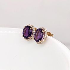 These stud earrings feature a pair of lovely purple natural, earth mined oval Amethyst in solid 14k gold with a natural diamond halo. These earrings can be a beautiful february birthstone gift for your loved ones!   Specifications  Item Type: Earrings Centre Stone: Amethyst Treatment: Heated Weight: 2/5.06 cttw Head size: 10x8mm Shape: Oval Hardness: 7  Metal: 14k/3.81g Diamond Clarity/Color: SI / G-H Diamond Count/Weight: 40/0.55 cttw  SKU: AJE120/2823  These earrings are made with solid 14k Go Chanel Stud Earrings, Pink Stud Earrings, Ruby Earrings Studs, Blue Stud Earrings, Gold Diamond Earrings Studs, Black Stud Earrings, Amethyst Studs, Sapphire Earrings Studs, White Gold Earrings Studs