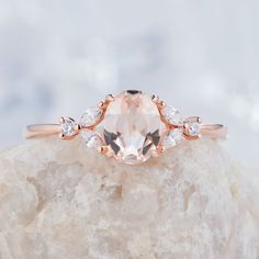 an oval morganite and diamond ring sitting on top of a rock