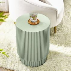 a round table with a glass on it in front of a white chair and rug