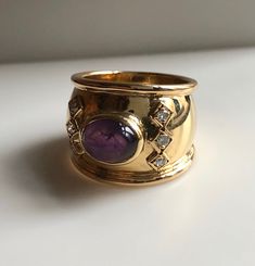 This is a beautiful statement ring. It features a vibrant purple amethyst Cabochon center stone with 6 round brilliant diamonds set in square boxes. The band is a nice thick width of 16.48mm. Amethyst is the birthstone of February. This cabochon cut Amethyst is a beautiful saturated lilac color. 1970s Vintage. Excellent condition. Metal:18k Yellow Gold. Weight: 9.47 grams Diamonds: .20ct size 9 With any pre-owned/Vintage/Antique items, it is common to have some wear, As we inspect each piece of Elegant Amethyst Cabochon Gemstones, Elegant Cabochon Amethyst Gemstones, Luxury Purple Cabochon Jewelry, Elegant Amethyst Cabochon Ring, Vintage Gemstone Cabochons For Anniversary, Classic Amethyst Cabochon Jewelry, Vintage Round Gemstone Cabochons, Luxury Purple Stone Jewelry, Luxury Purple Jewelry With Stones