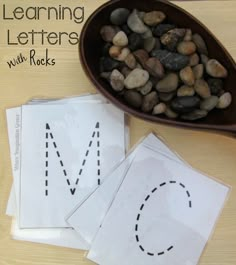 rocks and paper with the words learning letters on them next to a bowl of rocks