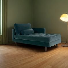 a blue chaise lounger sitting on top of a hard wood floor next to a lamp