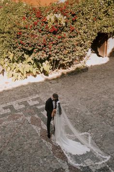 a bride and groom standing in the middle of a cobblestone road with red flowers