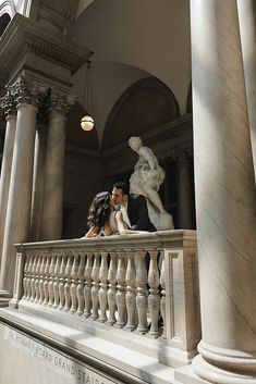 a man and woman standing on top of a balcony next to each other near columns