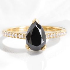 a black and white diamond ring on a white surface with diamonds around the band, set in 18k yellow gold