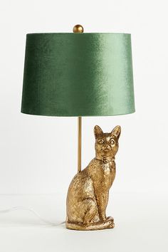 a gold cat lamp sitting on top of a table next to a green lampshade