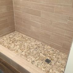 a tiled shower stall with stone flooring and brown tile on the walls, along with a drain in the middle