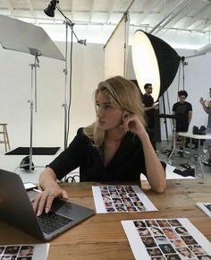 a woman sitting at a table with a laptop in front of her and people behind her