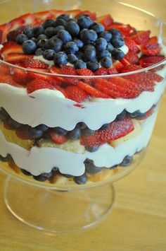 a trifle with strawberries and blueberries in it on a clear dish sitting on a wooden table