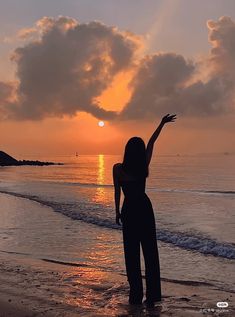 a woman standing on top of a beach next to the ocean under a cloudy sky